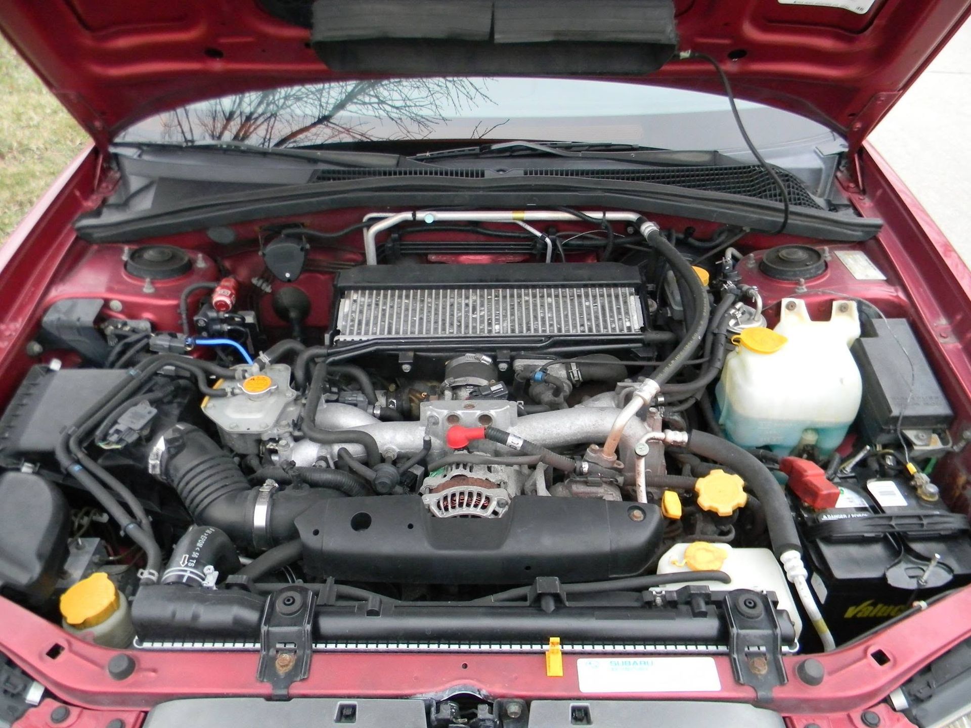 Car engine bay with hood open, showing hoses, reservoir, and radiator in a red vehicle.
