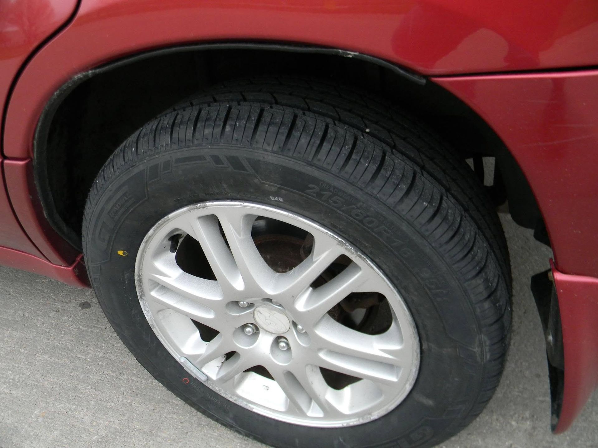 Close-up of a red car’s rear wheel and silver alloy rim on a road.