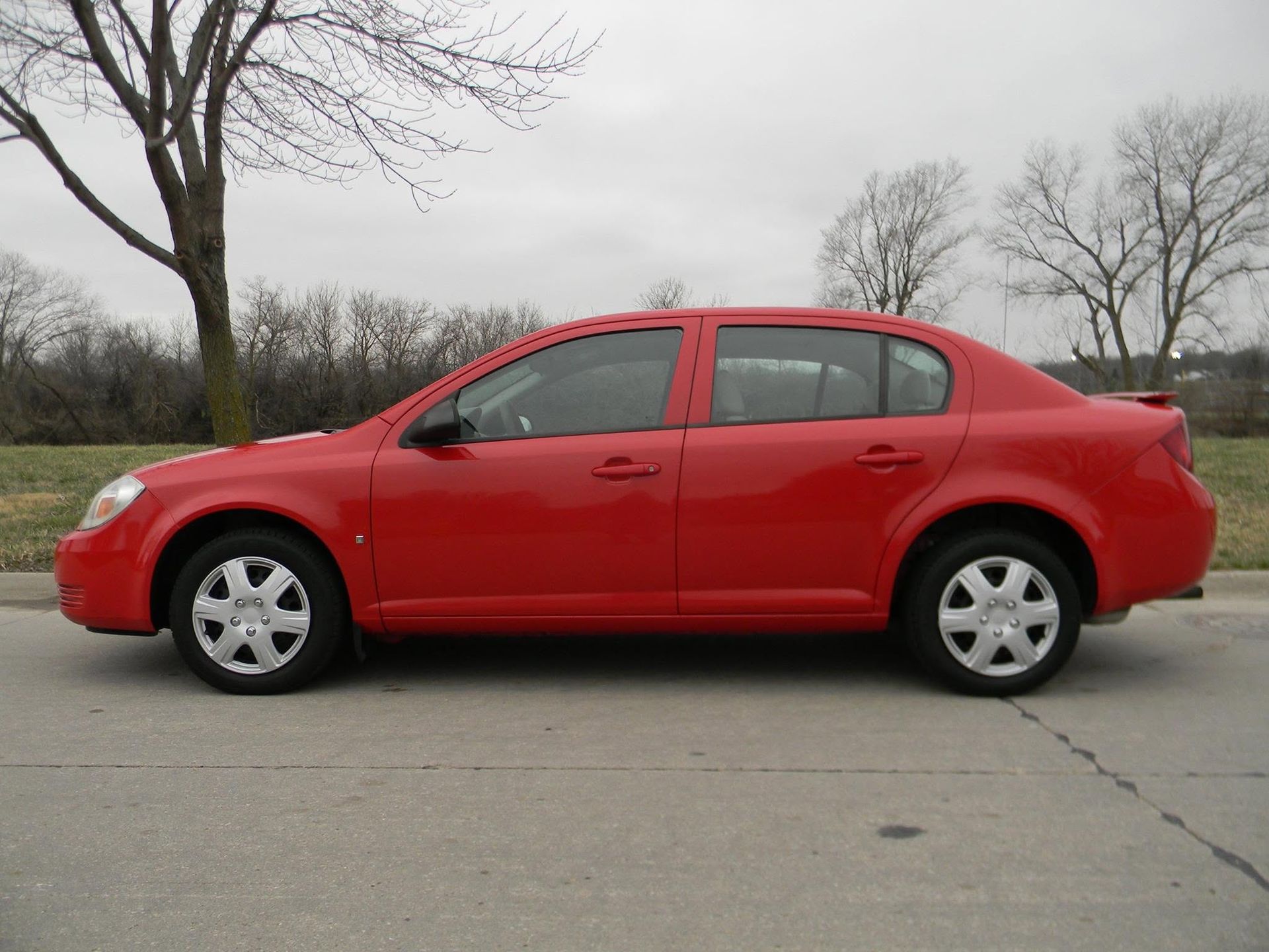 Red sedan parked on a roadside with leafless trees in the background