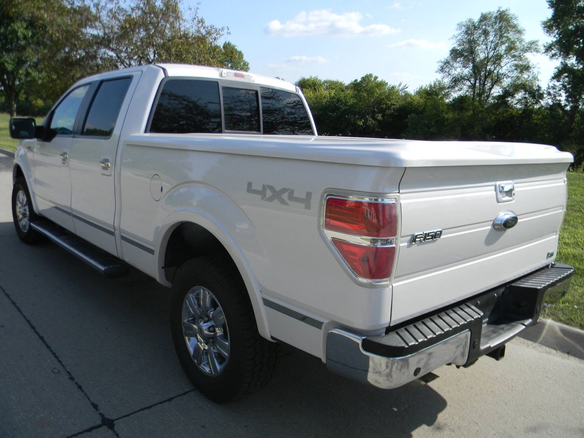 White Ford 4x4 pickup truck parked on a driveway, rear three-quarter view