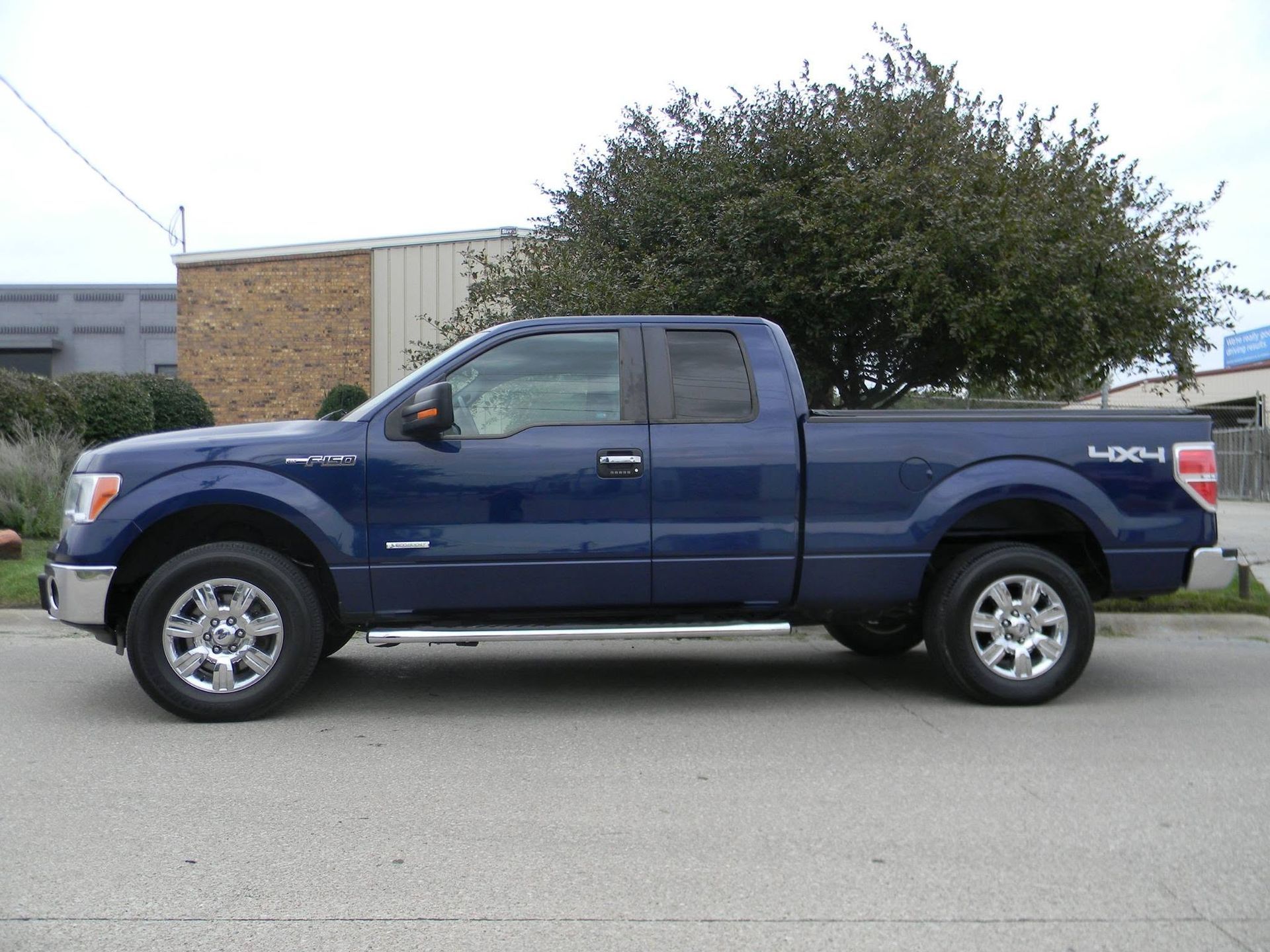 Blue pickup truck parked in front of a building and bushes