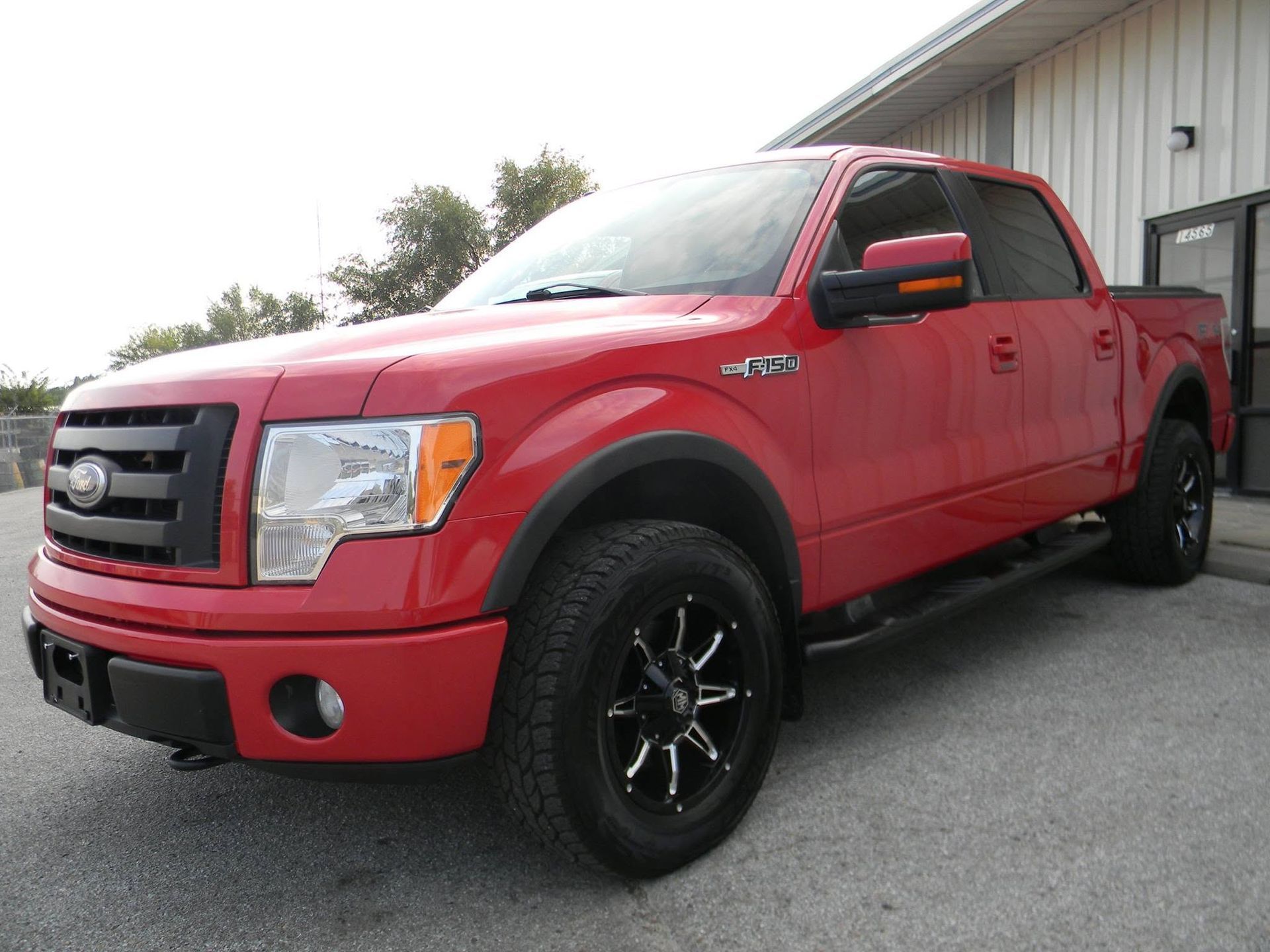 Red pickup truck parked beside a building on a paved lot