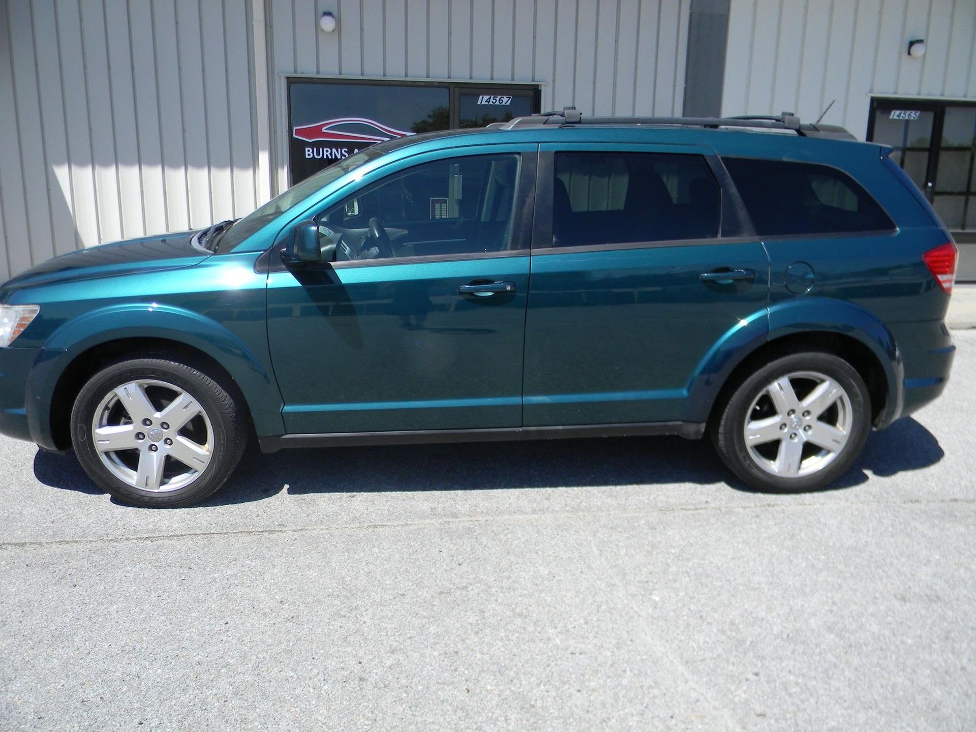 Teal SUV parked beside a building in bright sunlight
