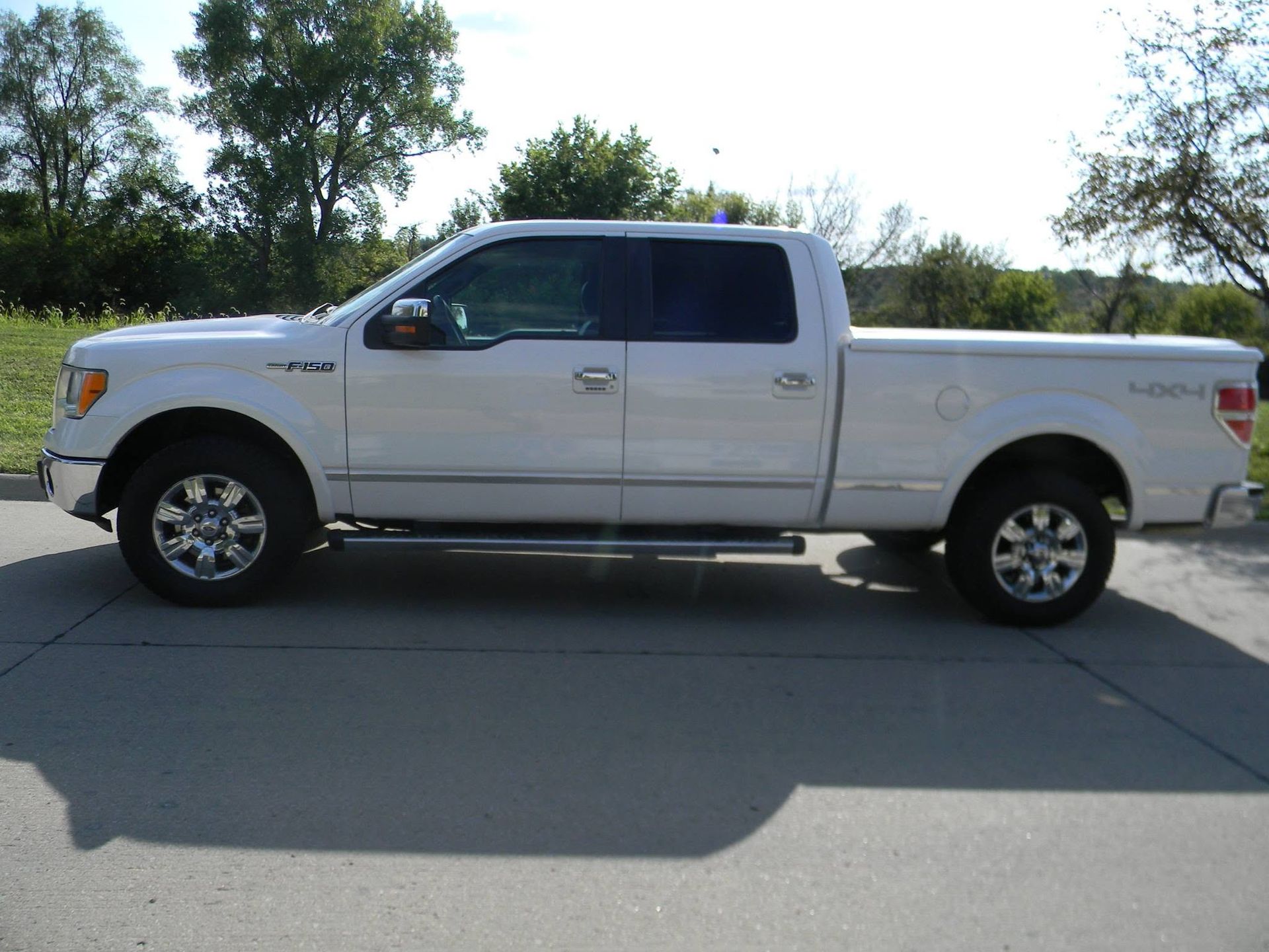 White pickup truck parked on a road beside trees and grass, side view