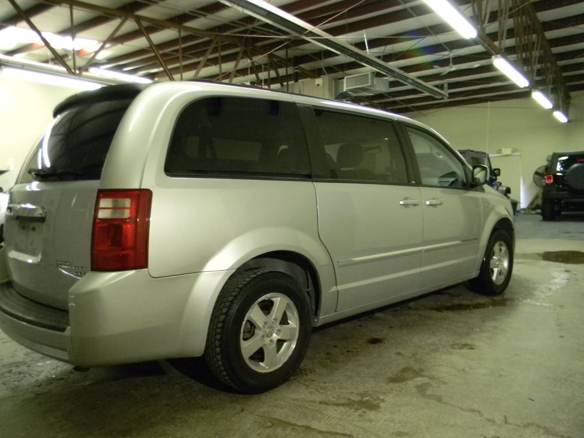 Silver minivan parked indoors in a dim parking garage, rear three-quarter view