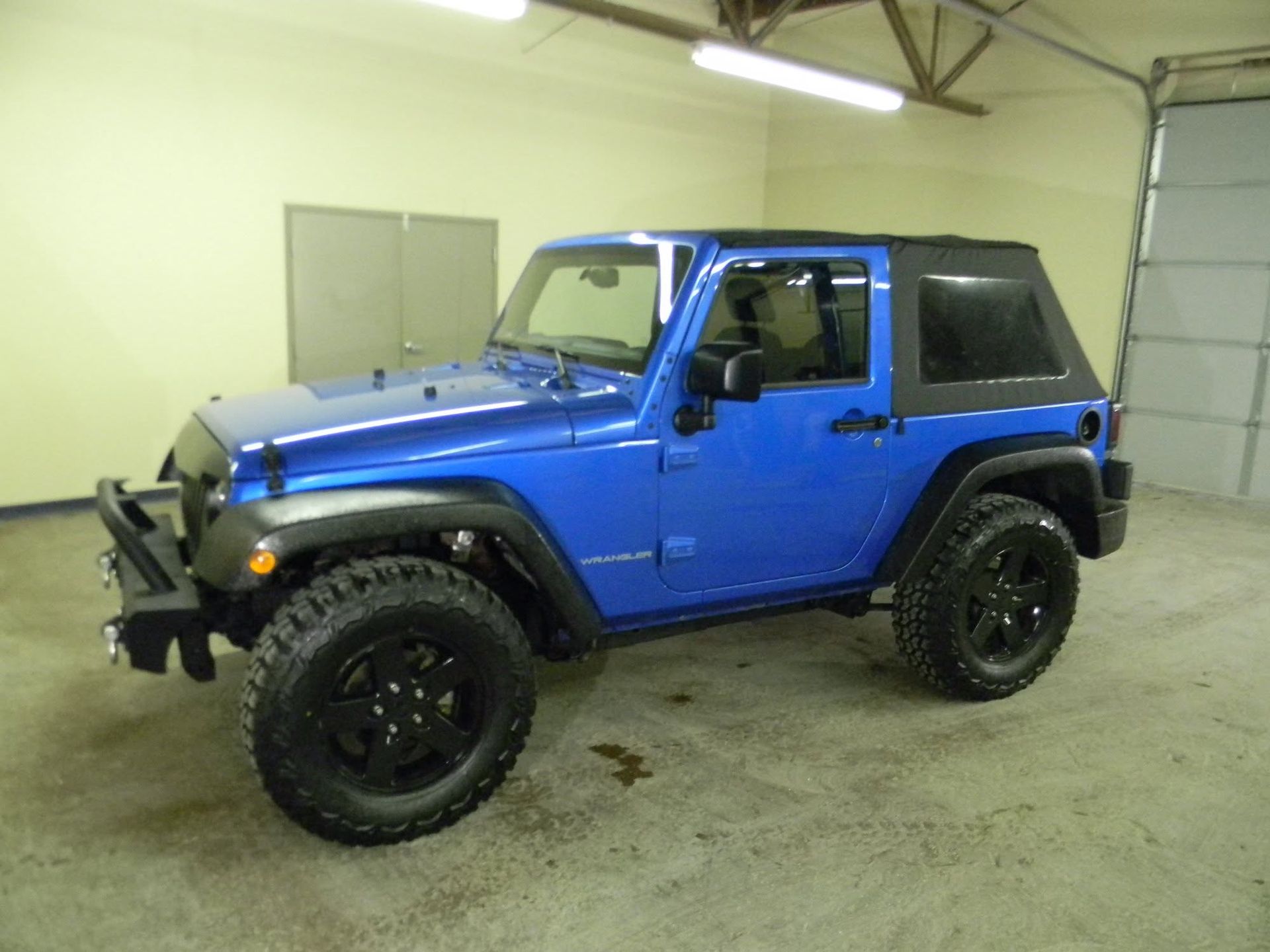 Blue off-road Jeep with black soft top parked indoors in a garage or showroom.