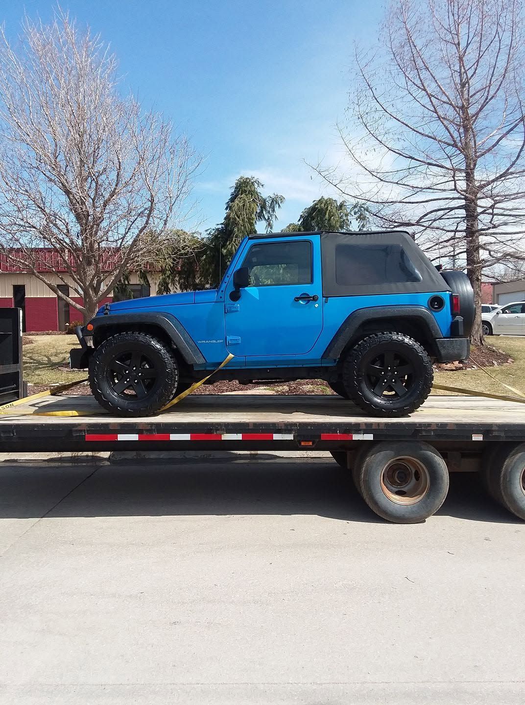 Blue Jeep Wrangler on a flatbed trailer in a suburban street.