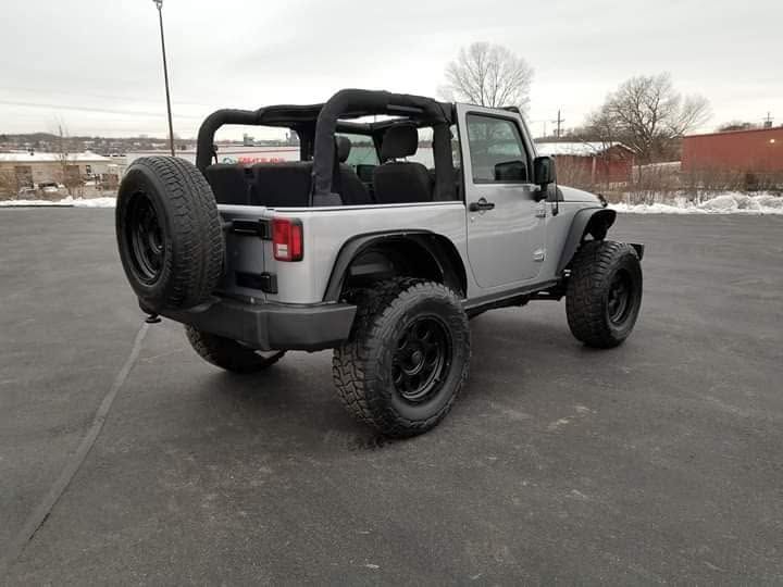 Silver Jeep Wrangler parked in a snowy lot, viewed from the rear-left side.