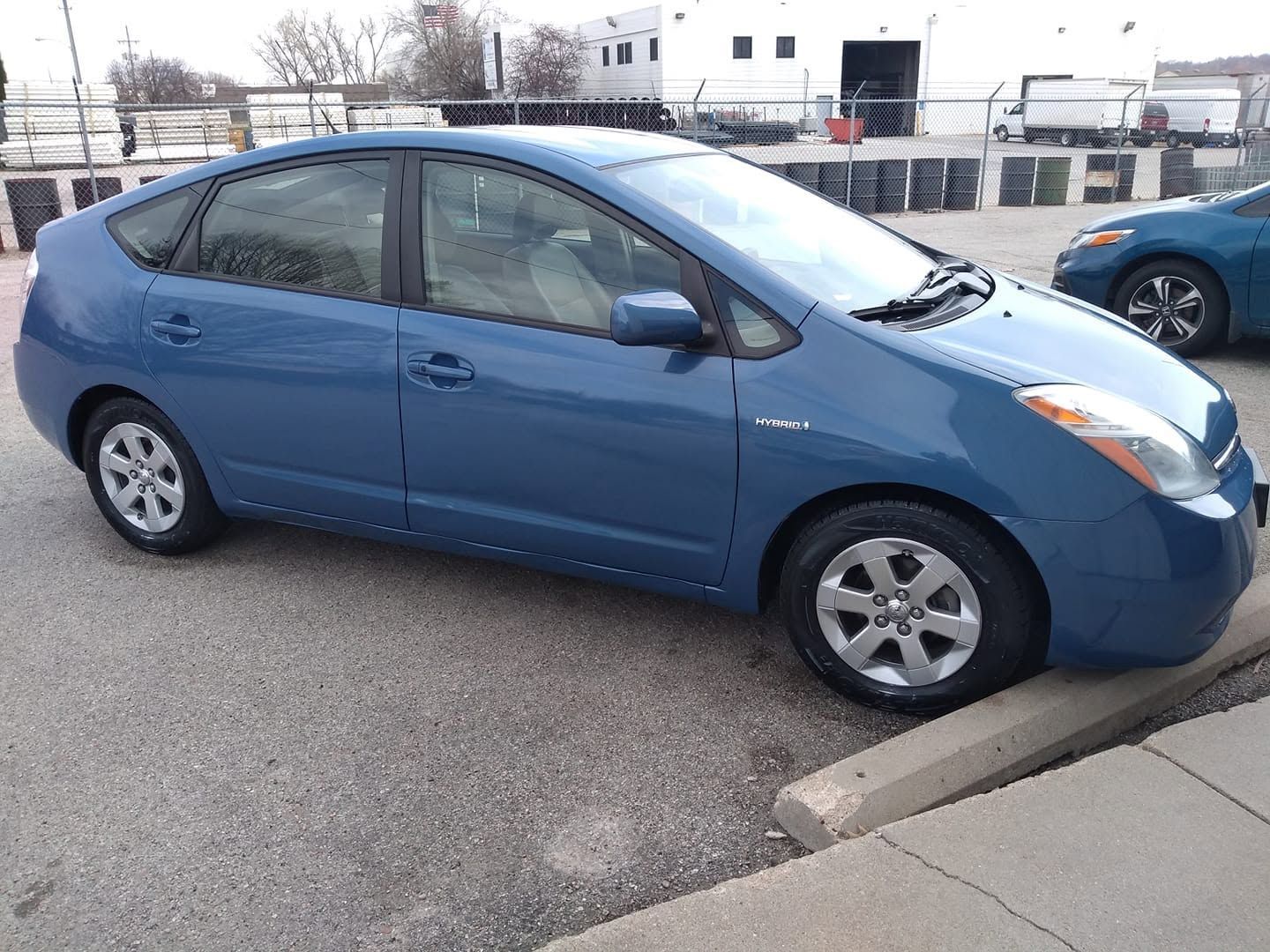 Blue Toyota Prius parked beside a curb in a lot on a cloudy day