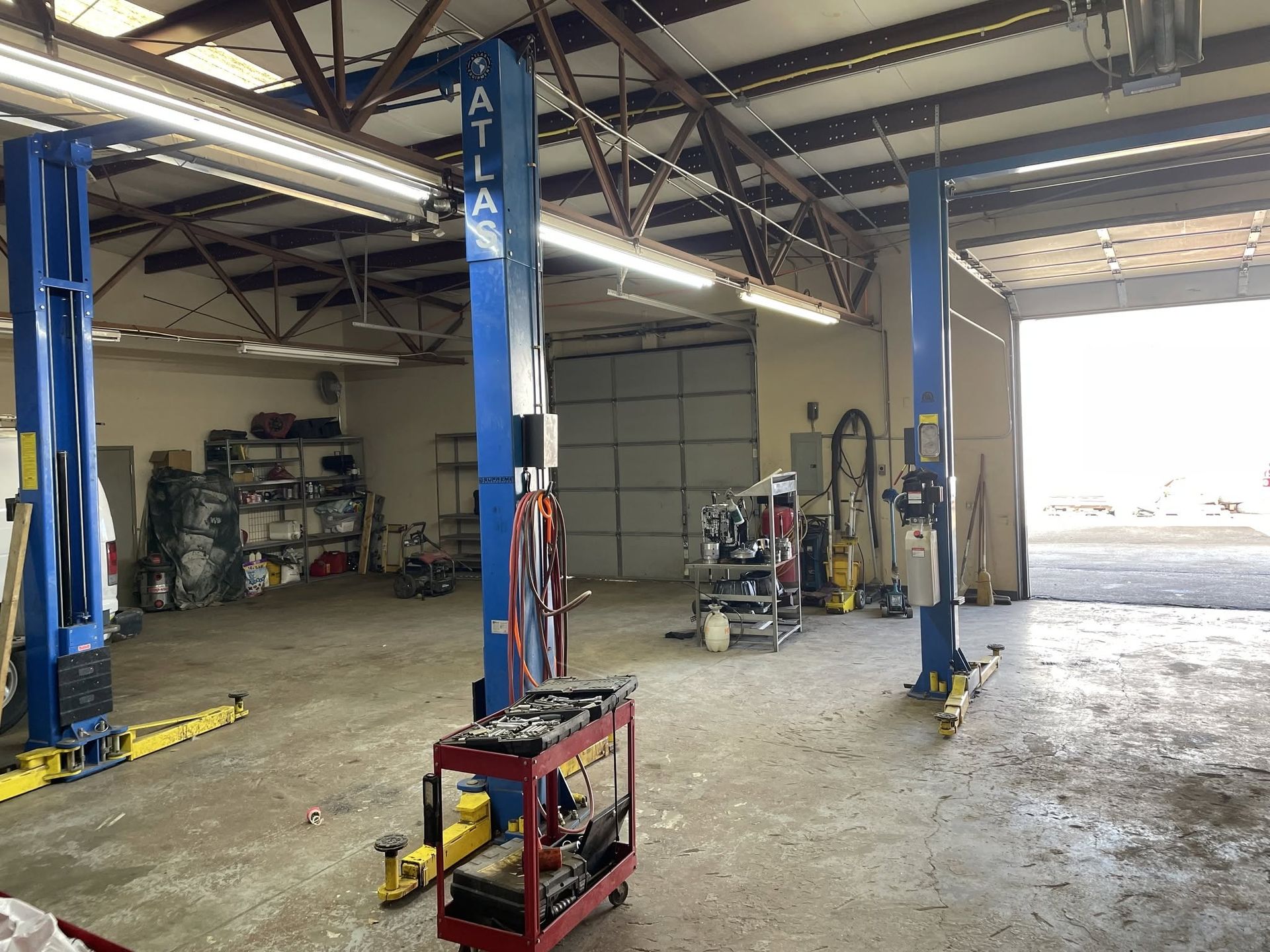Auto repair shop interior with two blue lifts, tools, and an open garage door to bright daylight