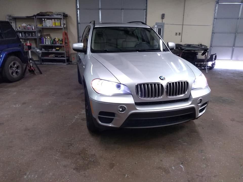 Silver BMW SUV parked inside a garage with shelves and a blue truck in the background