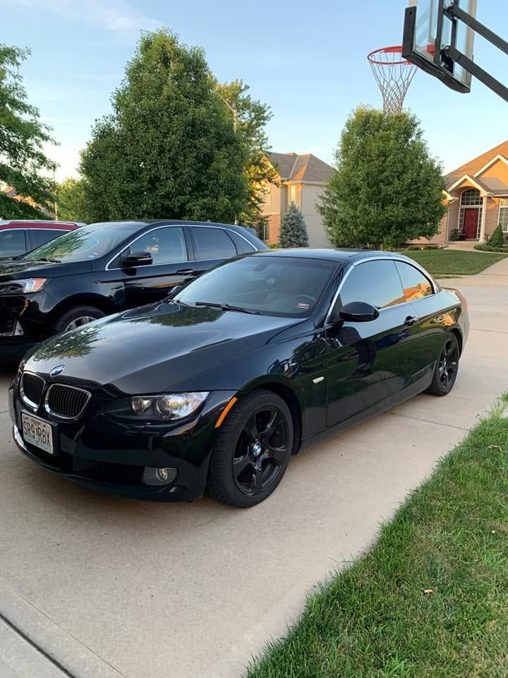 Black BMW coupe parked in a driveway beside a black SUV, with a basketball hoop overhead.