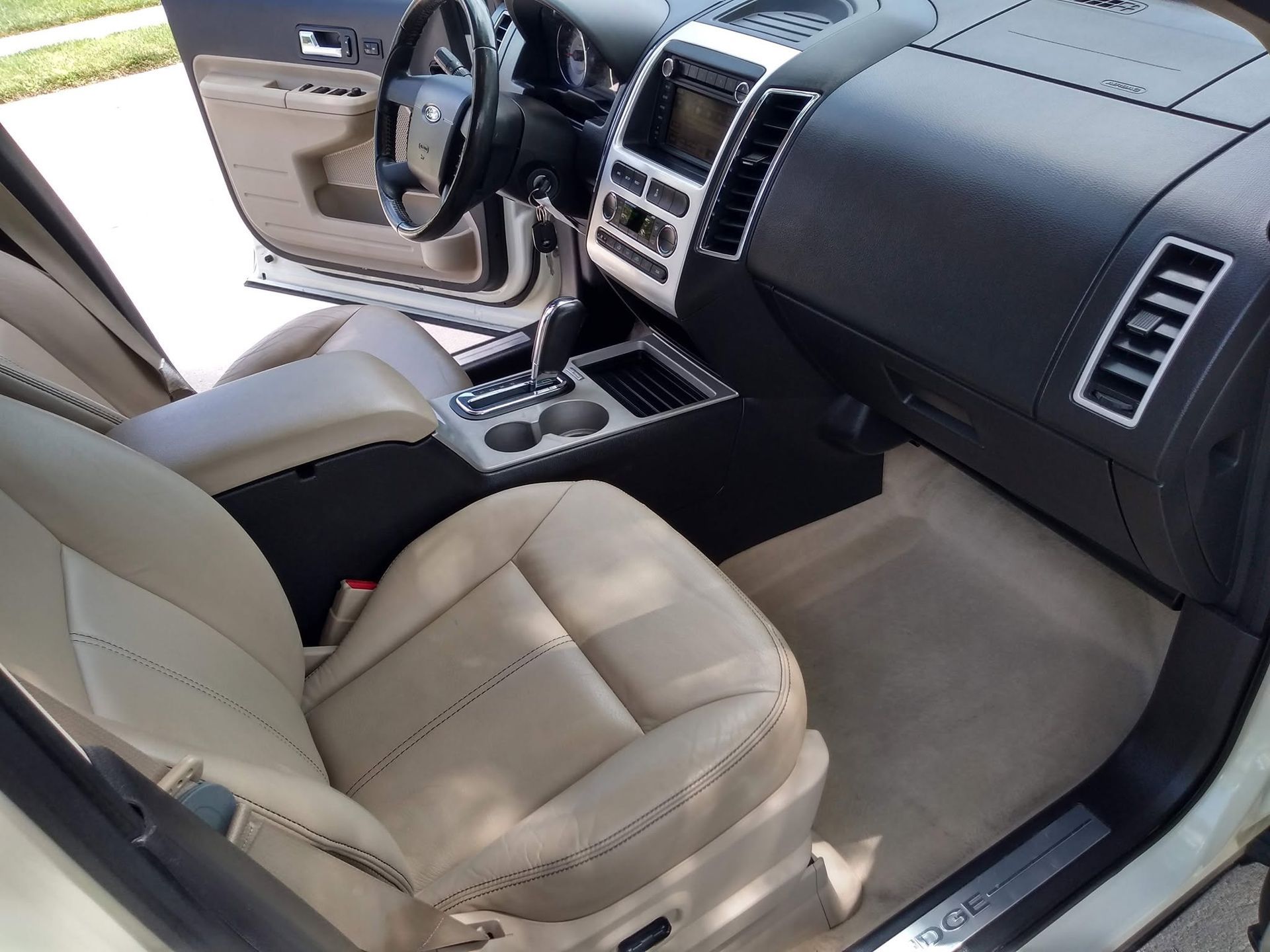 Tan leather car interior with open driver door, dashboard, and center console visible