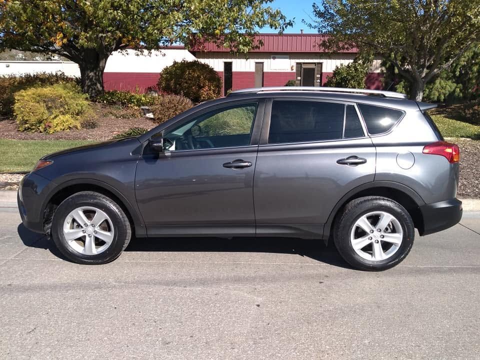 Gray SUV parked on a street in front of a building with trees and shrubs