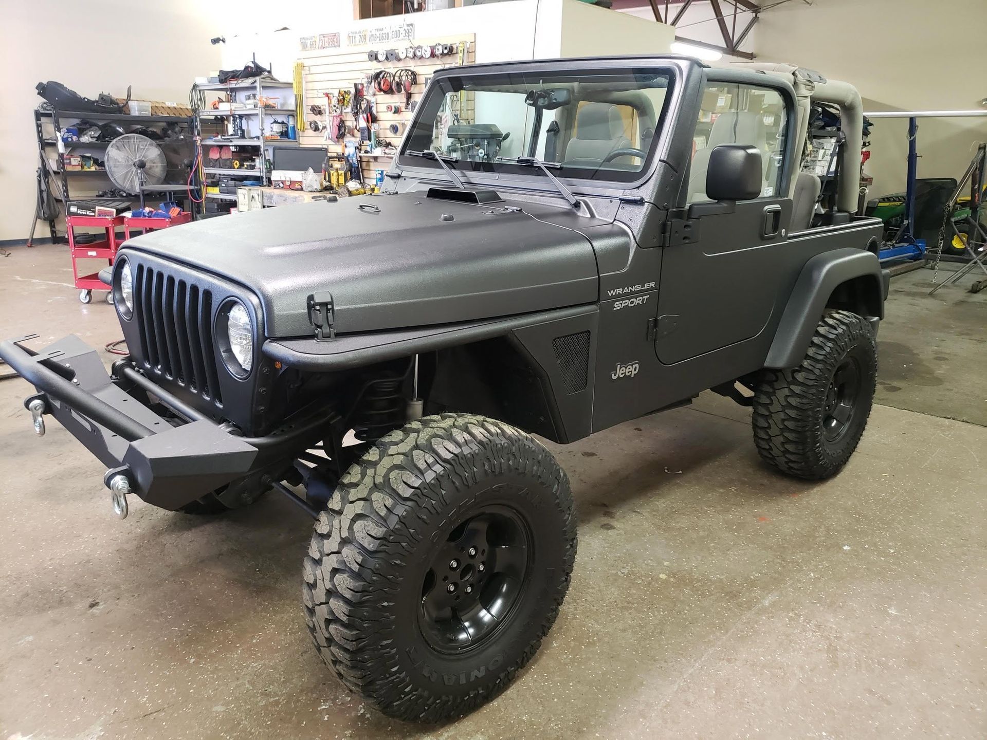Matte gray lifted Jeep Wrangler in a garage, with off-road tires and front winch.