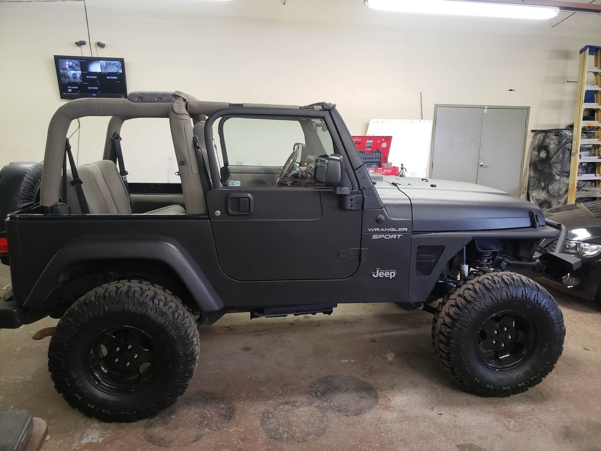 Black Jeep Wrangler with off-road tires in a garage, side view with open cabin and soft top removed
