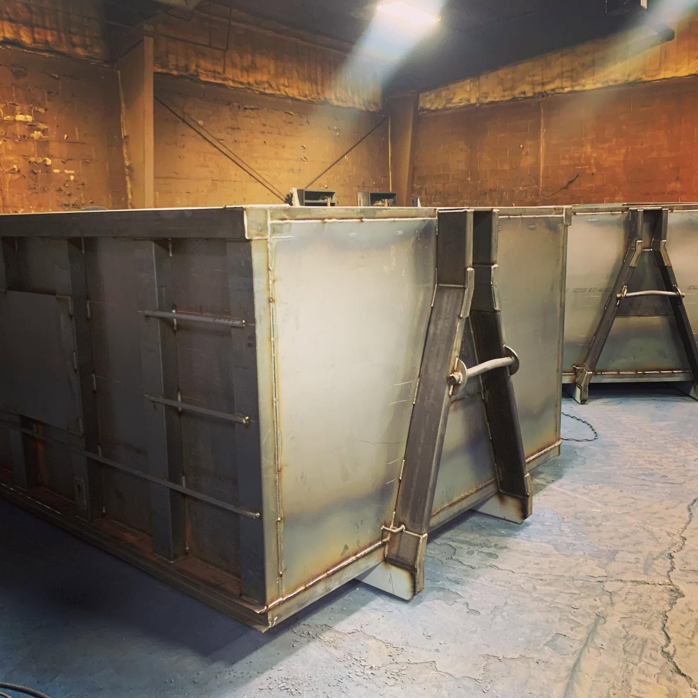 Large metal industrial molds or bins inside a workshop with concrete floor and rust-colored walls