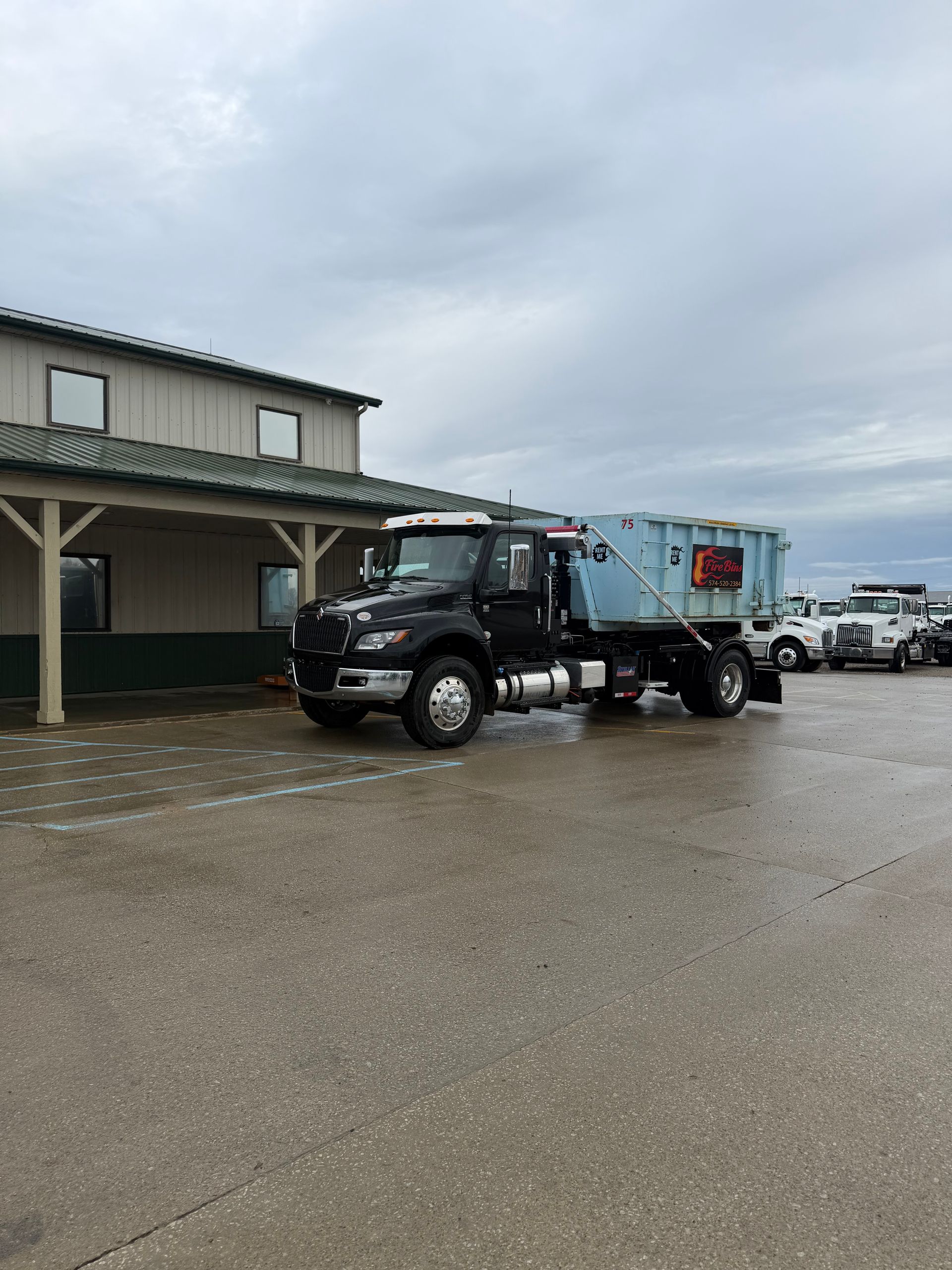Black dump truck parked beside a beige building on a wet, overcast lot