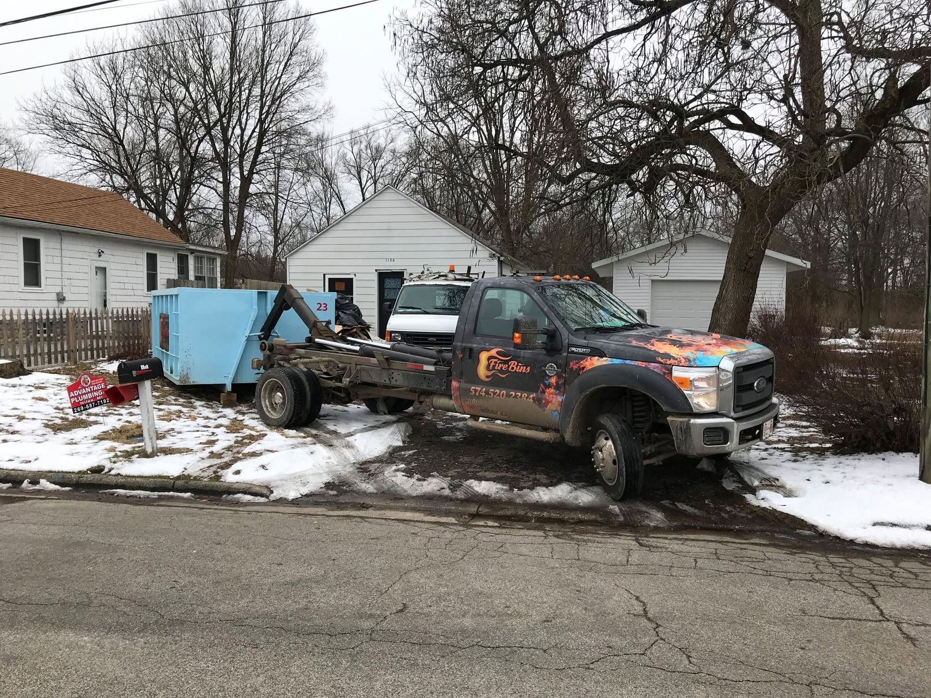 Pickup truck towing a blue trailer in a snowy suburban yard beside a house
