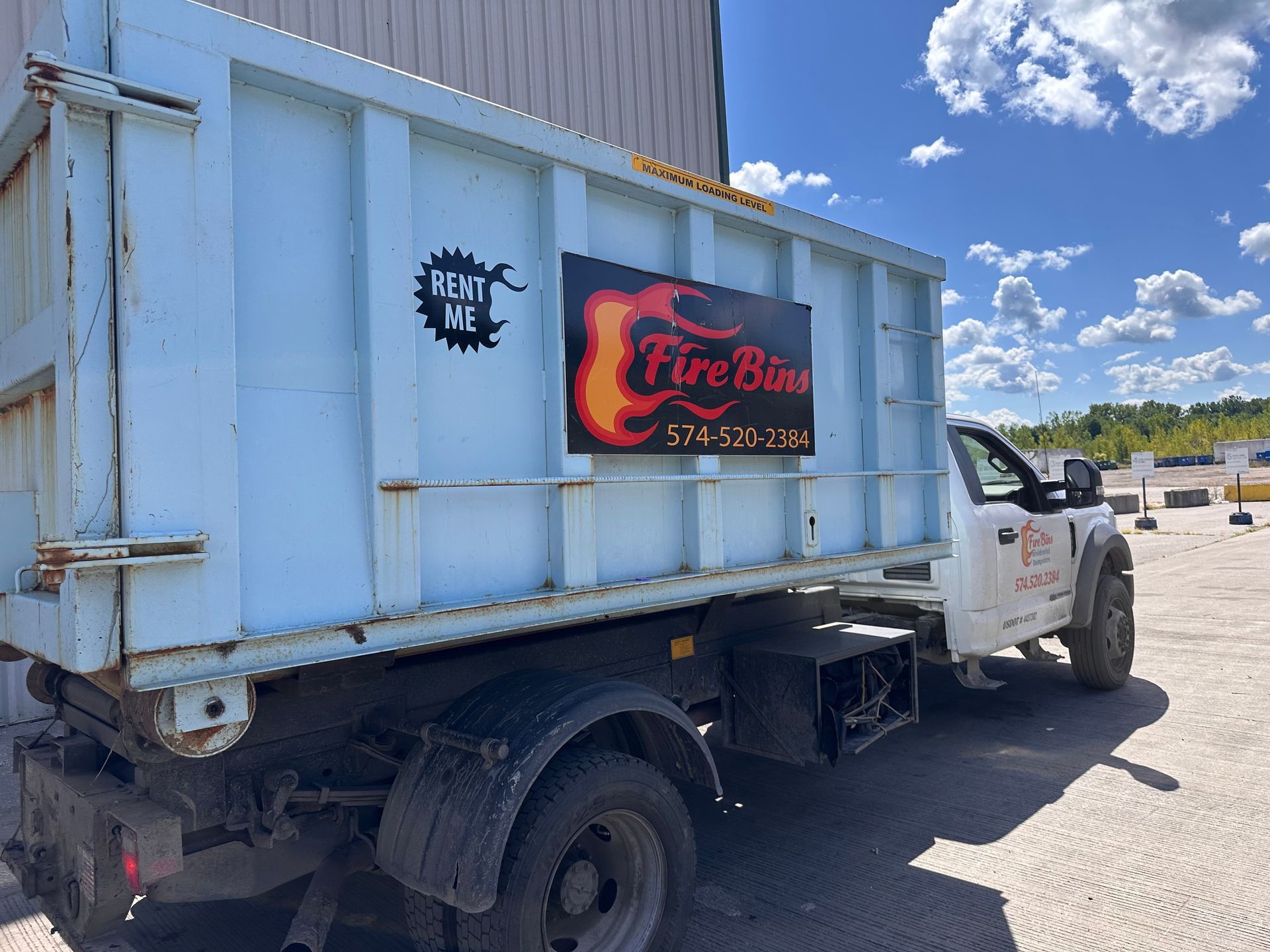 White pickup truck with a blue cargo box and fire-barbecue business sign parked outdoors under a blue sky