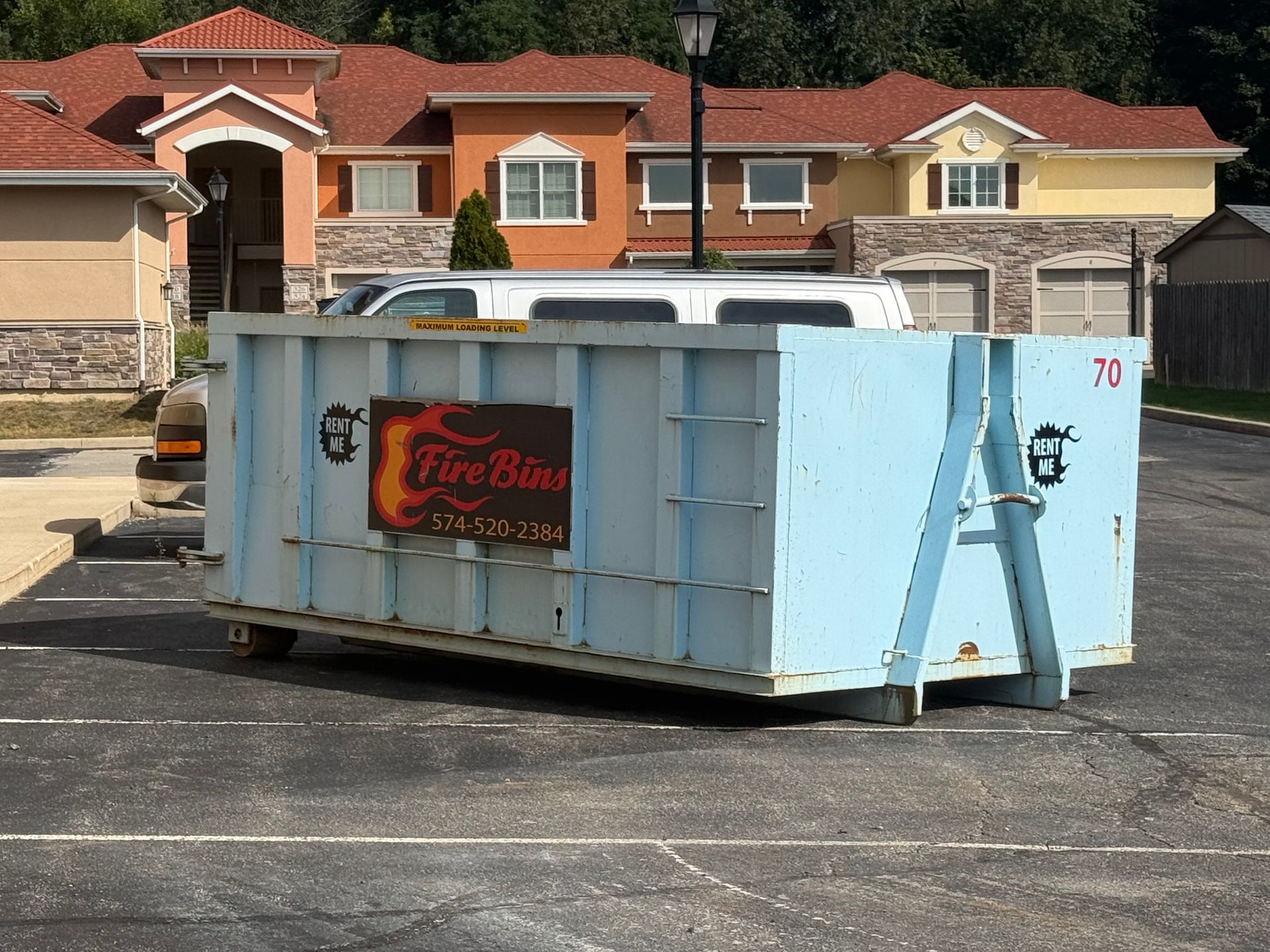 Light blue construction dumpster in a parking lot with houses in the background