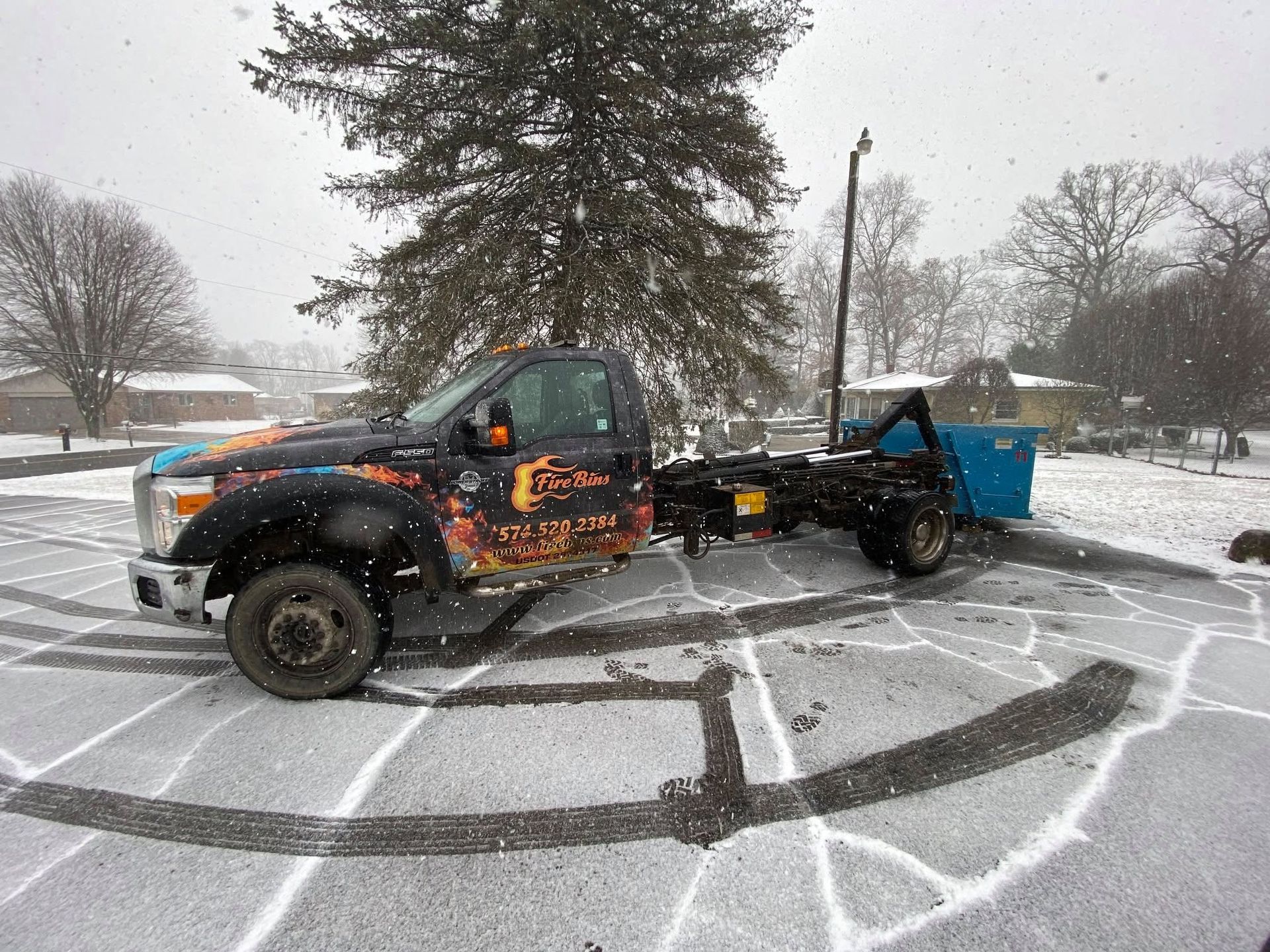 Tow truck hauling a blue dumpster through a snowy parking lot