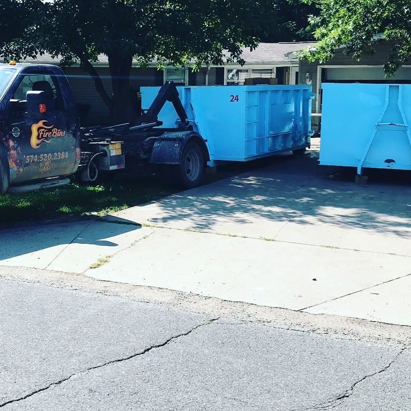 Tow truck hauling a blue dumpster on a residential street under trees