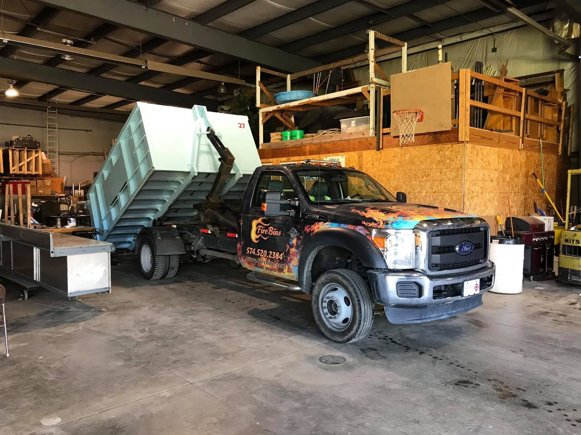 Dump truck loaded with debris inside a warehouse, with a dark pickup truck beside it.