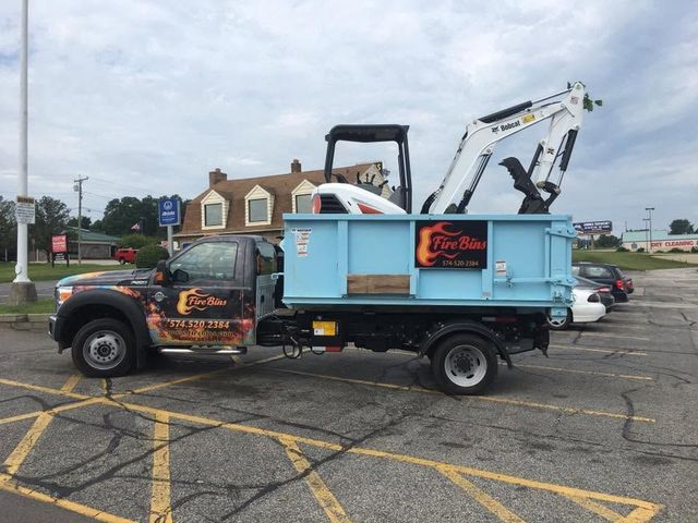 Dump truck with a folded mini excavator parked in a lot under a cloudy sky