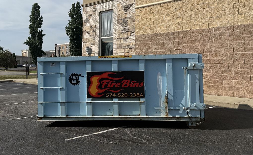 Light blue dumpster with Tire Barn sign outside a stone building on pavement