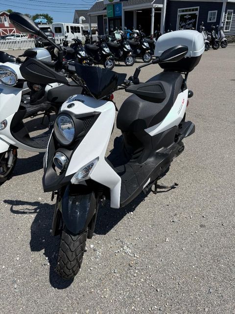 White and black scooter parked outdoors with several motorcycles in the background