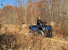 A man is riding a blue ATV through a field.