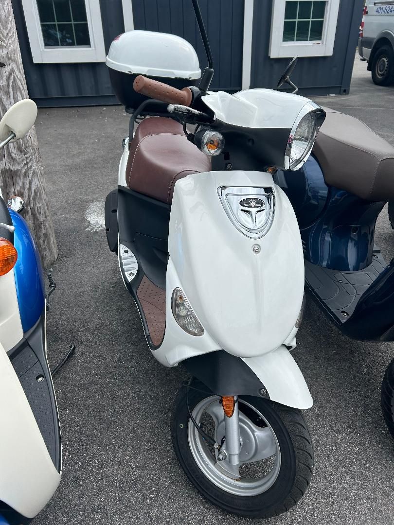 A white scooter is parked next to a blue scooter in a parking lot.
