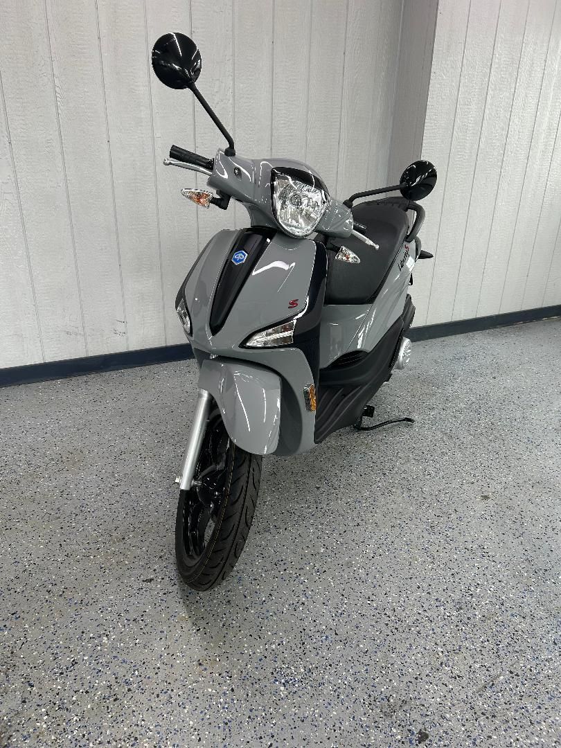 A gray scooter is parked on a concrete floor in a garage.