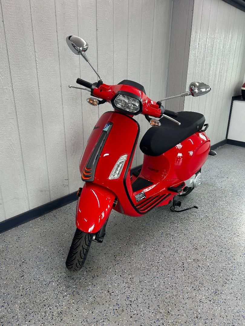 A red scooter is parked in a garage next to a wall.