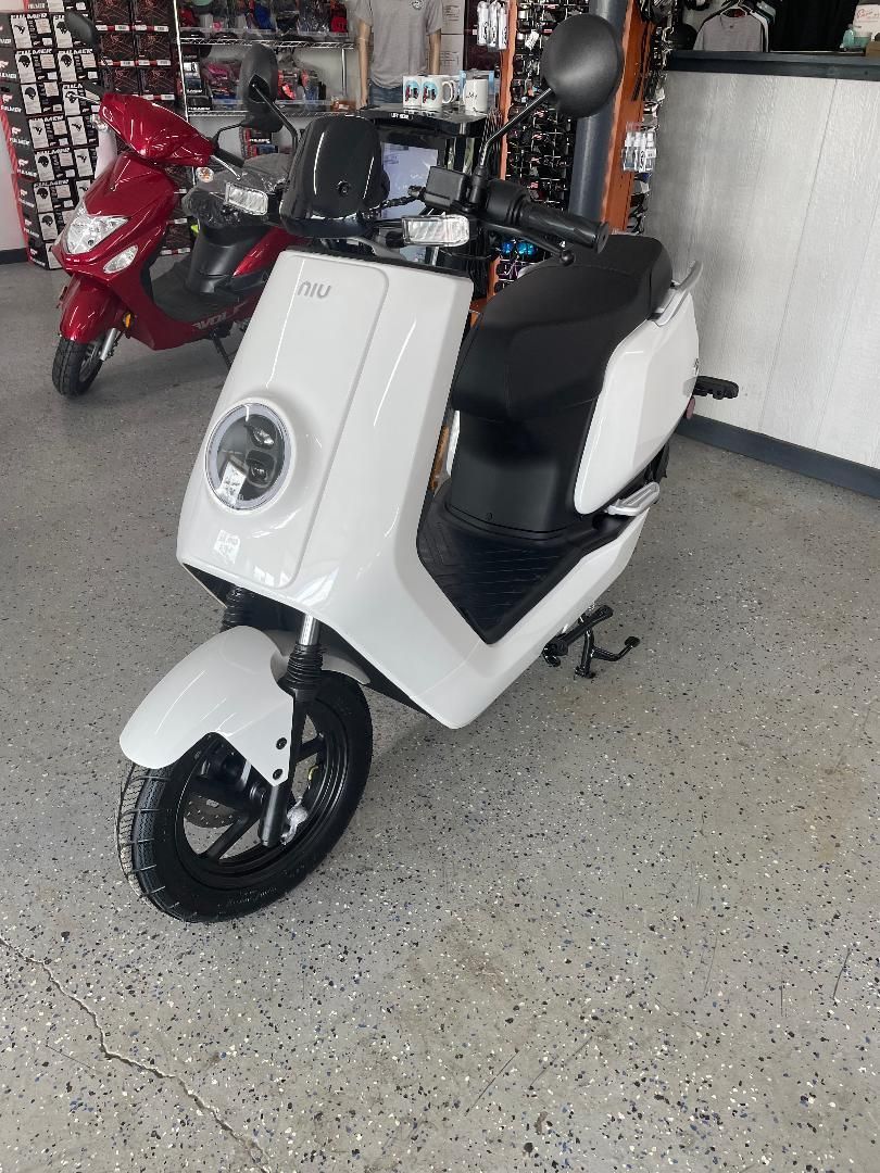 A white scooter is parked in a garage next to a red scooter.
