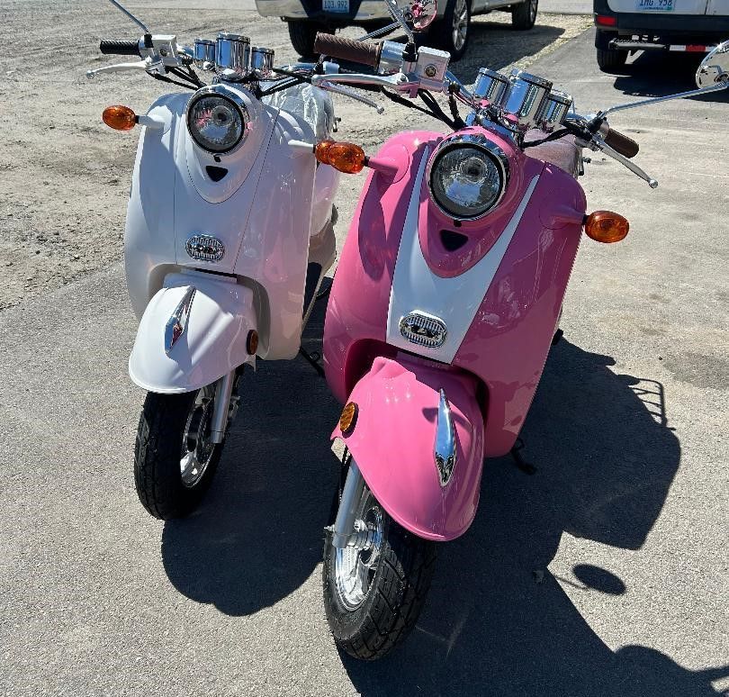 Two pink and white scooters are parked next to each other in a parking lot.