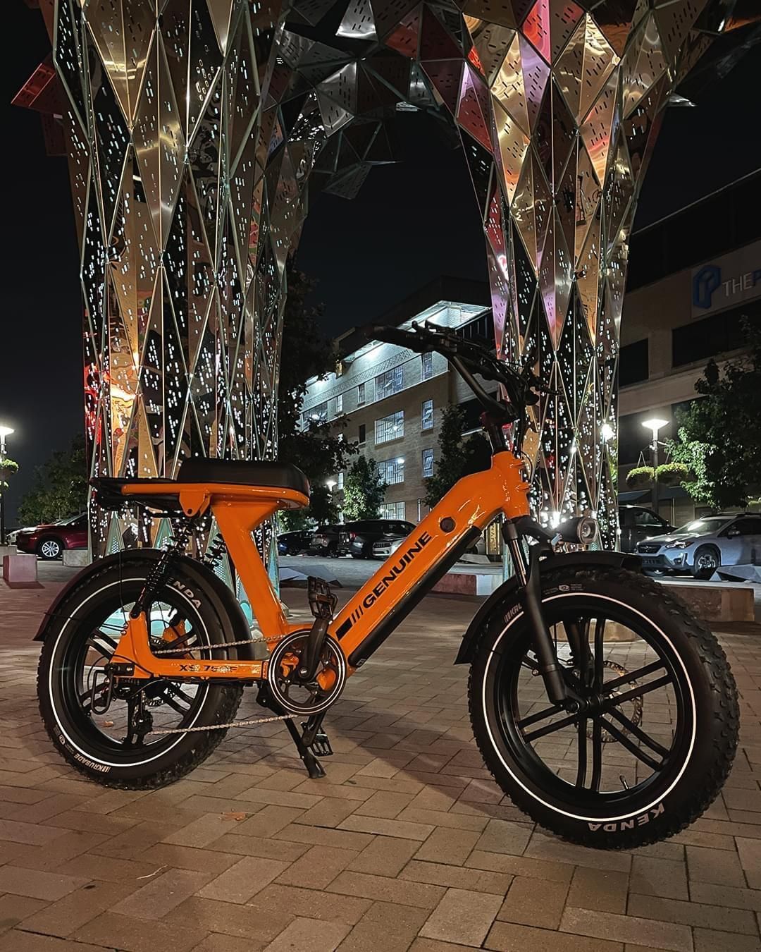 An orange bicycle is parked in front of a fountain at night.