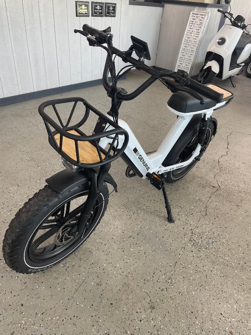 A white electric scooter with a basket on the front is parked in a garage.