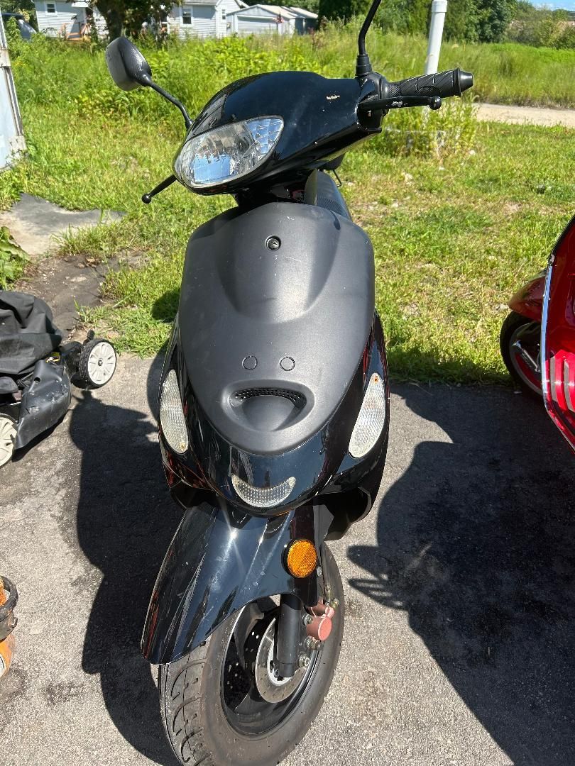 A black scooter is parked on the side of the road next to a red scooter.