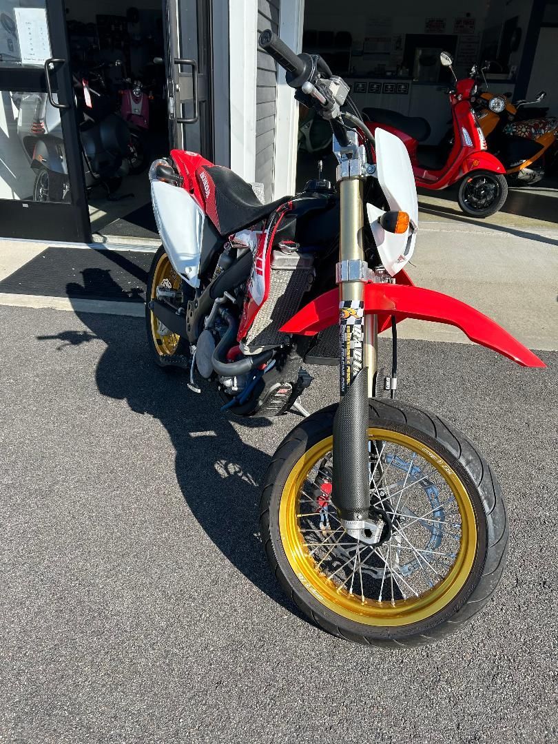 A red and white dirt bike is parked in front of a garage.