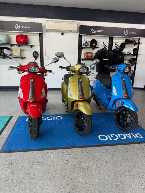 A dark blue Vespa scooter parked indoors on a light-colored, speckled concrete floor.