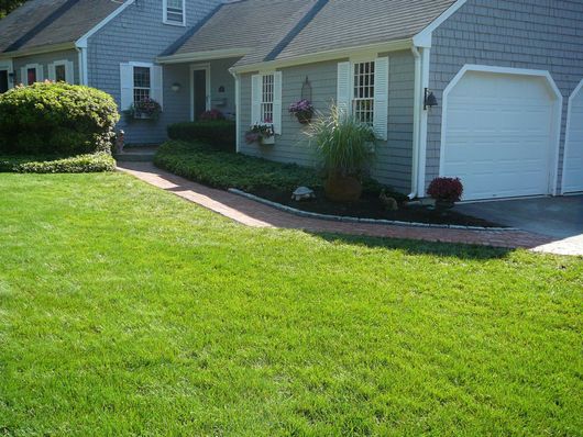 Suburban house with white garage doors, green lawn, and landscaped front walkway
