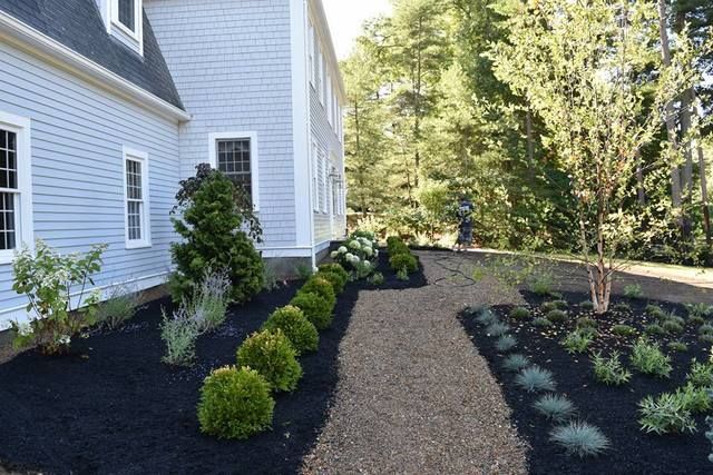 Landscaped yard beside a white house with mulch beds, shrubs, and a gravel path