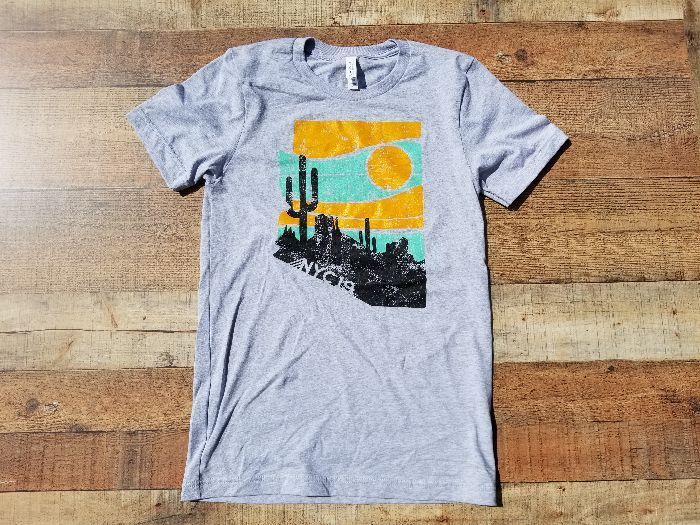 a grey t-shirt with a cactus and sun on it is sitting on a wooden table