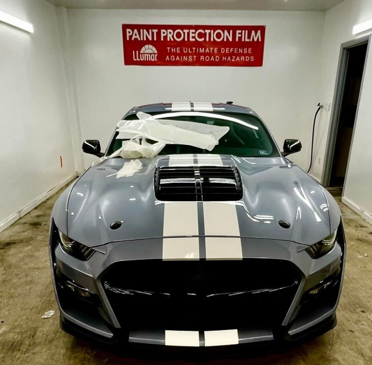 A gray mustang is sitting in front of a sign that says paint protection film.