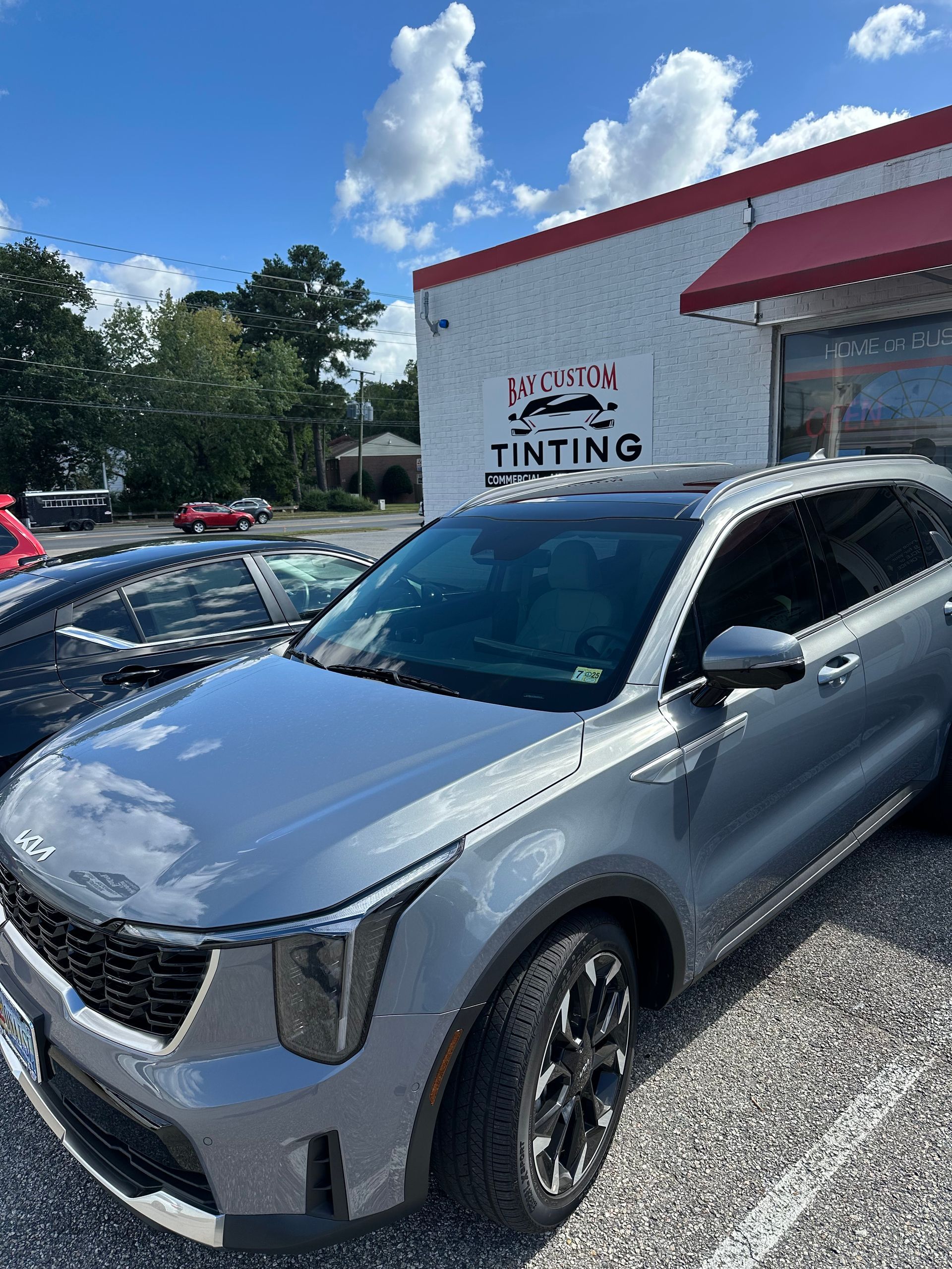 A silver car is parked in front of a car tinting shop.