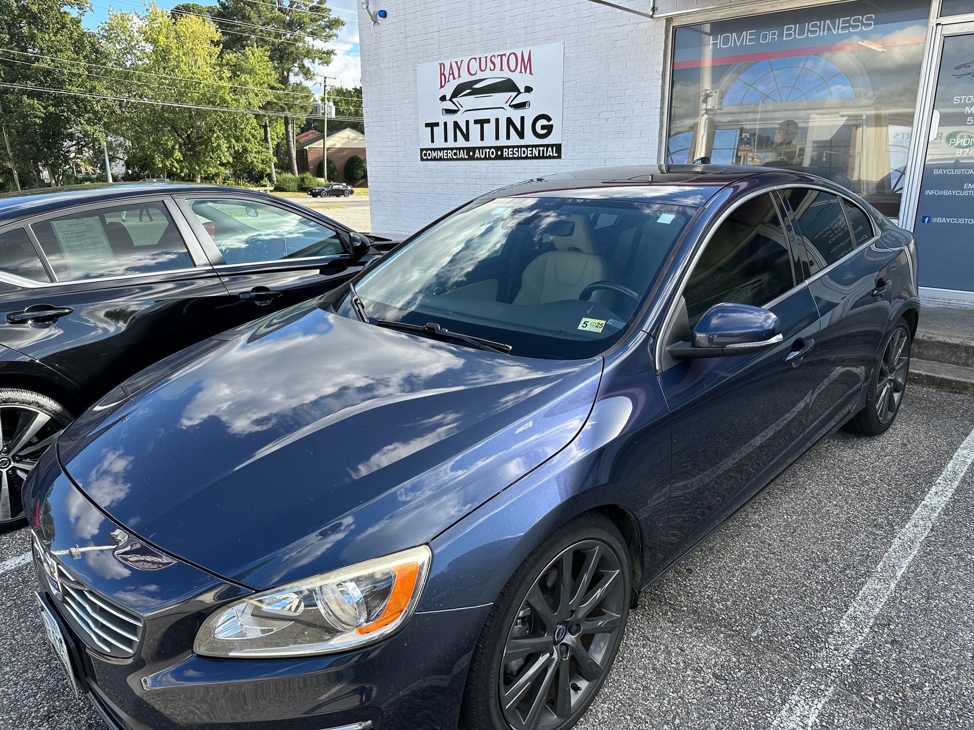 A blue car is parked in front of a tinting shop.