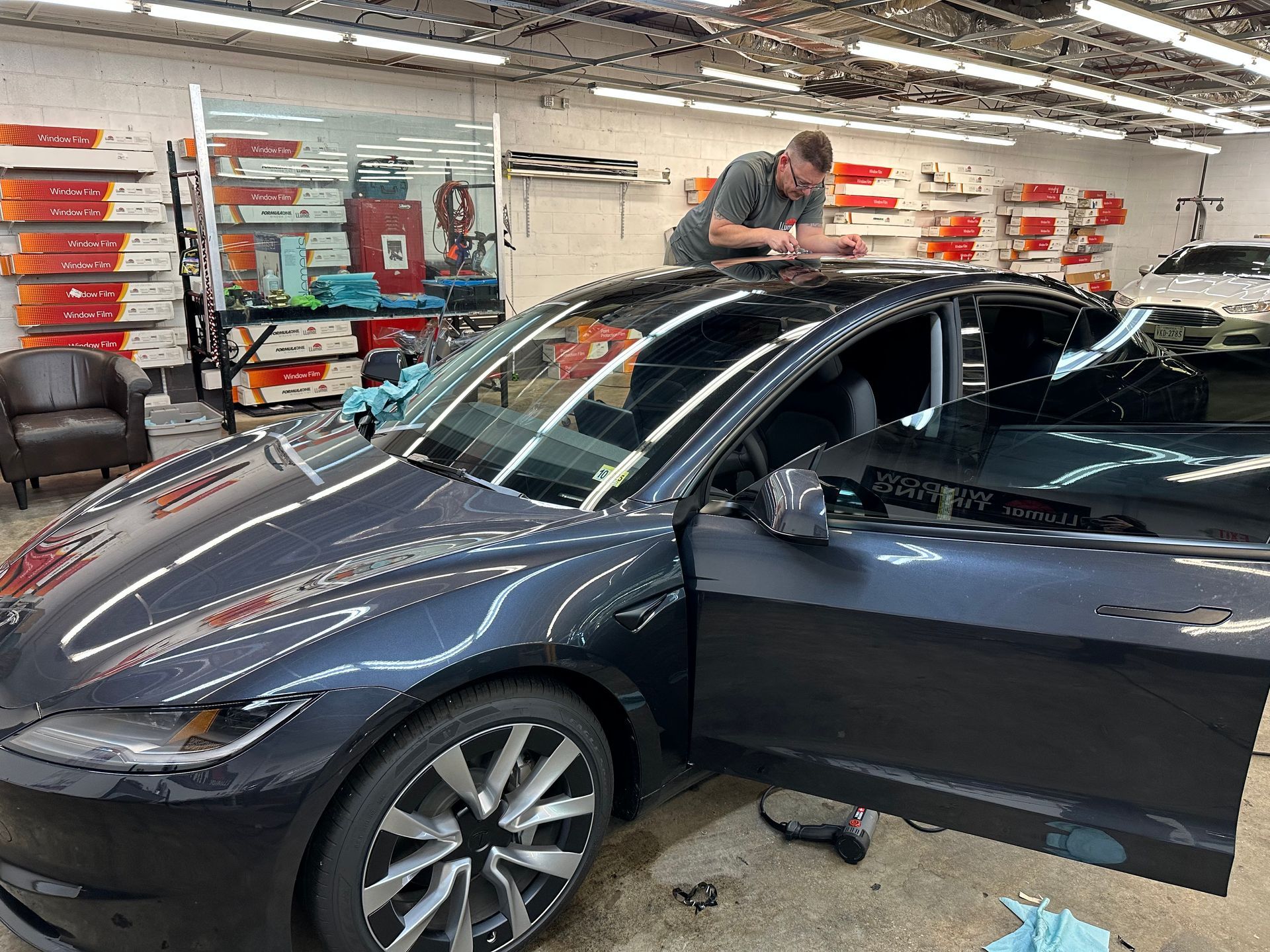 A man is working on the roof of a tesla model y in a garage.
