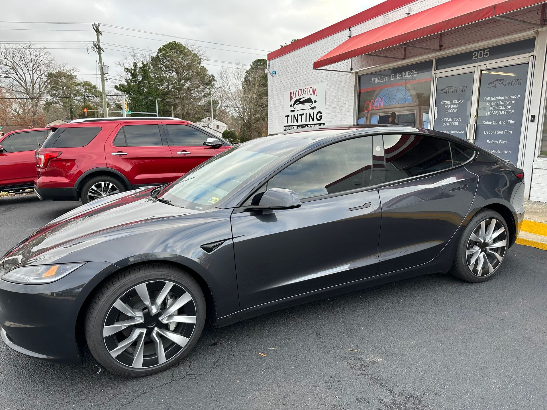 A black tesla model 3 is parked in front of a building.